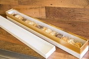 A long white and gold box containing assorted cookies displayed on a wooden surface.